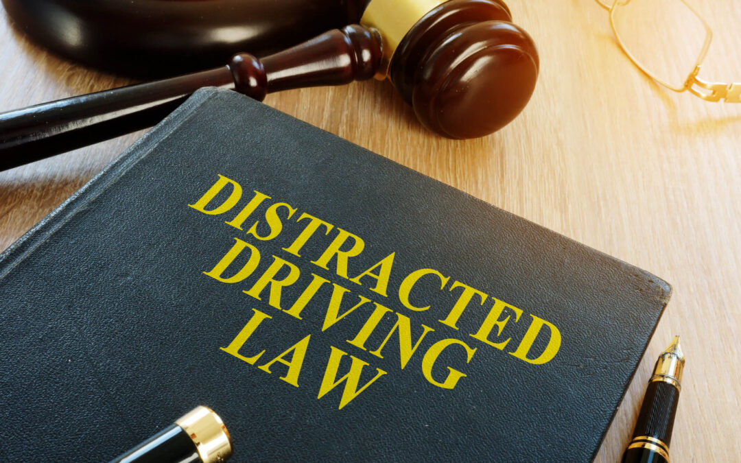 A black book with the words Distracted Driving Law printed on the front cover lays on top of a desk next to a gavel and block.